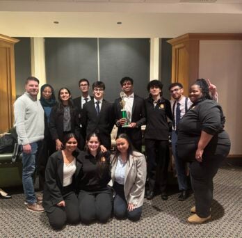 Team members and coaches of the UIC Mock Trial team smile, while holding a green trophy
                  