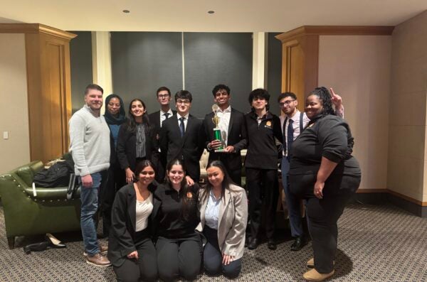 Team members and coaches of the UIC Mock Trial team smile, while holding a green trophy